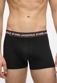 Černé bavlněné boxerky s hnědým elastickým pasem, na kterém je bílé logo "KARL LAGERFELD". Přiléhavý střih s detaily šití.