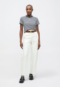 Tricou scurt, cu dungi bleumarin și alb, asortat cu pantaloni albi, cu talie înaltă. Cintură maro cu accesorii aurii, mocasini negri cu accente aurii.