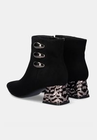 Botas de tobillo de ante negro con puntera afilada, tres acentos metálicos en el lateral y tacones metálicos de estampado leopardo con una forma única.