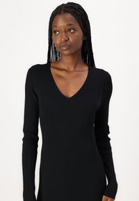 Black ribbed knit dress with a deep V-neck, long sleeves, and a fitted silhouette, highlighting vertical texture and seamless design details.