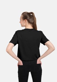 Camiseta negra de manga corta con cuello redondo, diseño simple y color sólido. Lleva pantalones negros y se ve desde la parte de atrás.