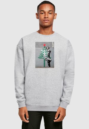 Grå sweatshirt med et trykt design af en dreng, der rækker ud efter en stjerne på toppen af et grønt træ med en rød stjerne, sat mod en tekstureret baggrund.