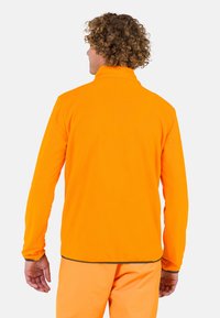 Orangenes Fleece-Jackett mit hohem Kragen, langen Ärmeln und kontrastierenden Nähten. Weiche Textur, minimalistisches Design und abgerundeter Saum.