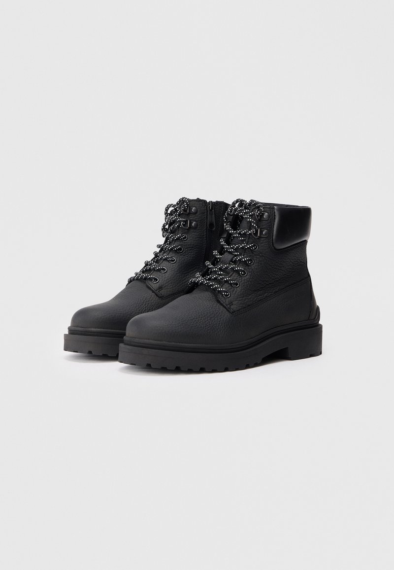 Black leather ankle boots with a textured finish, featuring round shoelaces and a thick, rugged sole for traction. Zipper on the side.