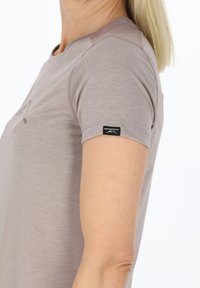Lys brun t-shirt med korte ærmer i et blødt, ribbet stof. Har et logo foran og et mærke med "SWEDIRNOUNT" på ærmet.