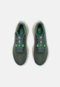 Green sports shoes with a textured mesh upper, padded tongue, and grey sole. Features reflective accents and a logo on the tongue.