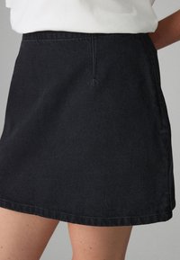 Gonna svasata in denim nero con tessitura liscia, vita diritta e cuciture a contrasto lungo l'orlo e le cuciture.