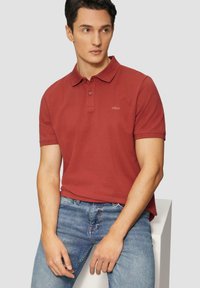 Polo-shirt rouge en coton avec un col, deux boutons et des manches courtes. Associé à un jean en denim bleu et à une texture tactile.