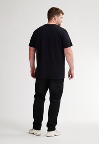 Camiseta de algodón negra con mangas cortas, corte holgado y escote redondo, combinada con pantalones vaqueros negros y zapatillas deportivas blancas.
