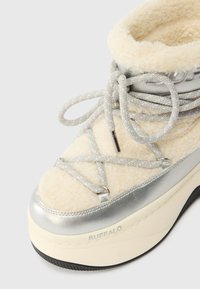 Buffalo platform sneaker har en overdel af kremfarvet skjul med sølvmetalliske accenter, grå snørebånd og en tekstureret sort gummisål.