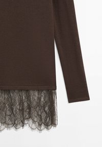 Hnědý pletený top s dlouhým rukávem a tmavě hnědým květinovým krajkovým lemem sahajícím pod lem na bílém pozadí.