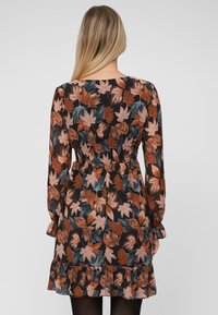 Bloemenjurk met lange mouwen, zwarte achtergrond en bruine en groene bladerenpatronen. Fijne taille en gerimpelde zoomdetails. Zachte stof.