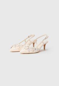 Ivory krūšu atbalsta papēži ar norādītu purngalu, rotāti ar slāņveida ziedu akcenteiem un nelieli rhinestones. Iezīmējas ar slaidu papēdi un potītes siksniņu.