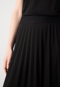 Mustat laskostetut hameet, joissa on ribbattu vyötärö, valmistettu pehmeästä materiaalista, jossa on toonikkapinta ja pystysuorat taitteet.