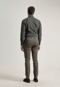 Camisa verde oscura de manga larga, diseño ajustado; combinada con pantalones entallados de color gris claro. Zapatos marrones, vista desde atrás.