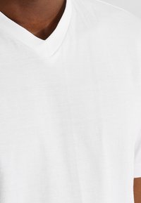 T-shirt blanc à col en V fabriqué en tissu doux. Présente un design épuré avec une texture lisse et des coutures minimales.