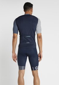 Herrcykeloutfit bestående av en marinblå tröja med randiga korta ärmar och en blixtlåsficka, kombinerat med åtsittande marinblå shorts och mönstrade detaljer.