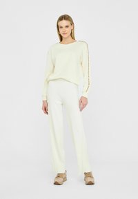 Set di abbigliamento da casa di un crema chiaro lavorato a maglia, composto da un top a maniche lunghe con dettagli di bottoni dorati sulle maniche e pantaloni a gamba larga con coste abbinati.