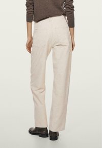 Light beige, corduroy wide-leg pants with back pockets and a high waist, paired with a brown sweater and black ankle boots.