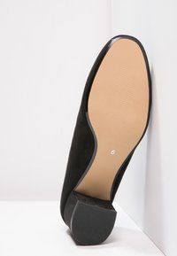 Black suede high heel shoe with a rounded toe, textured outer surface, and a smooth tan rubber sole showing size 6 marking.