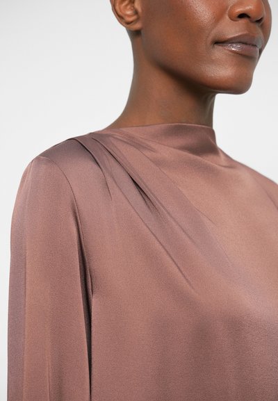 Blouse en satin marron avec un col montant et des plis sur les épaules, texture lisse et drapé élégant.