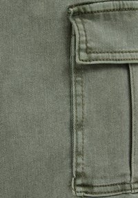 Maslinasto zelena denim tkanina s dodatkom džepa. Tekstura je blago gruba, s vidljivim šavovima i suptilnim twill uzorkom.
