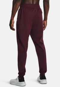 Pantalones deportivos burdeos con cintura elástica, bolsillos laterales y piernas ajustadas, combinados con zapatillas blancas con diseño perforado.