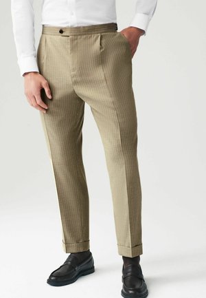 Pantalons rayés kaki avec un design à plat, texture de tissu lisse, associés à des mocassins noirs, dotés d'un ourlet légèrement retroussé.