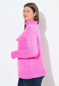 Pull en tricot rose à col montant, avec une coupe décontractée, présentant des poignets et un ourlet côtelés. Texture douce avec un motif de tricot épais.