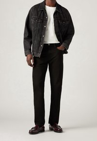 Chaqueta de denim negra sobre una camisa blanca, combinada con pantalones negros y mocasines burdeos. Los detalles notables incluyen bolsillos delanteros y cierres de botón.
