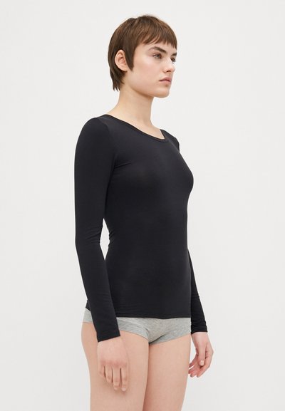 Black long-sleeve top made of smooth, stretchy fabric with a round neckline, paired with gray shorts, modeled by a person.