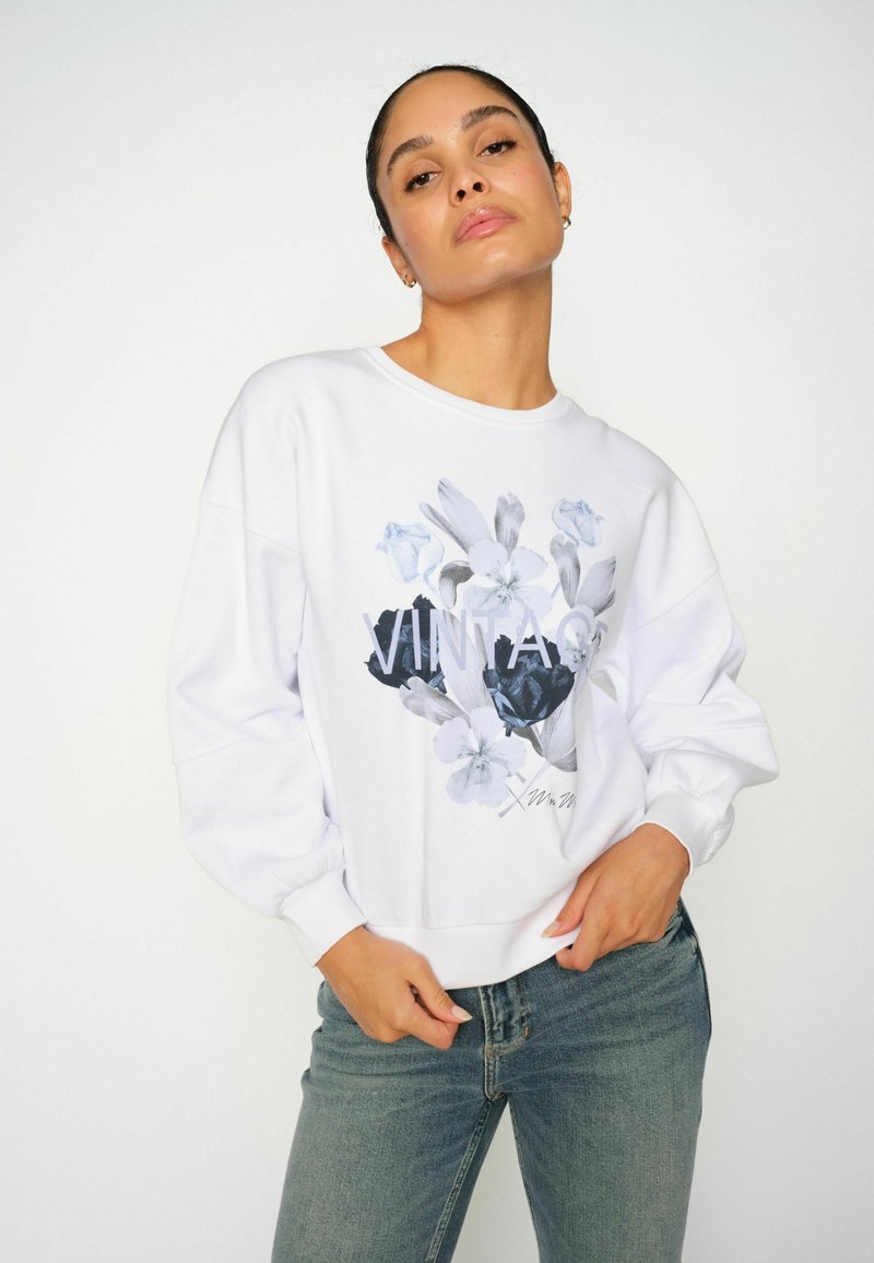 Sudadera blanca con un estampado floral que presenta flores negras y azules. Corte relajado, cuello redondo y mangas largas con volumen.