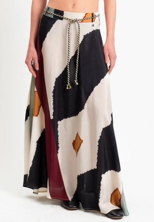 Vista dalla vita in giù di una persona che indossa una gonna a portafoglio con motivo nero, bianco, arancione e bordeaux, con cintura di corda e scarpe nere.