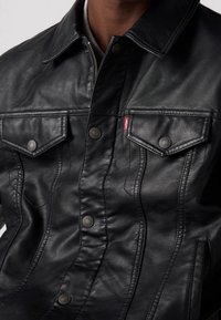 Giubbotto di pelle nera con due tasche sul petto con bottoni a pressione, dettagli di cucitura in evidenza e un design classico del colletto.