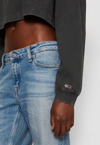 Mörkgrå cropped sweatshirt med ribbade muddar, kombinerad med ljusblå denimjeans med blekt tvätt och en logotypapplikation på fickan.