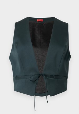 Tmavozelená bezrukávová vesta s hlbokým výstrihom do V, tenkým predným zaväzovaním a čiernym vzorovaným vnútorným lemom, rozložená na bielom pozadí.