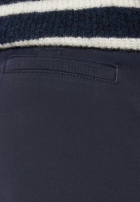 Tissu bleu marine avec une texture lisse et une poche arrière. Un pull rayé en tricot blanc et bleu foncé partiellement visible au-dessus.