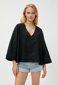 Schwarzes Leinenoberteil mit V-Ausschnitt und weiten Dreiviertelärmeln. Das Design ist locker geschnitten und wird mit hellblauen Jeansshorts kombiniert.