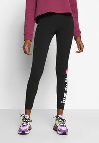 Svarta leggings med en åtsittande design, prydda med en vit "just do it"-grafik på sidan. Bärs med en lila ribbad tröja och färgglada sneakers.