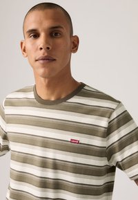 Ριγέ κοντομάνικο T-shirt σε ελιά και λευκό χρώμα, με ριμπ λαιμόκοψη και μικρό κόκκινο λογότυπο Levi's στο στήθος.