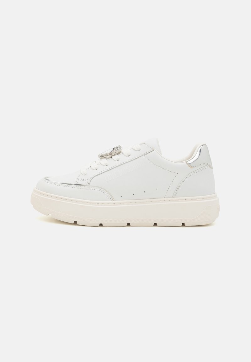 Baskets en cuir blanc avec une semelle épaisse, des accents argentés, un logo sur le côté, et un design perforé sur le panneau extérieur.