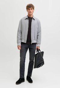 Gray bomber jacket with ribbed cuffs, black textured sweater, dark jeans, and black leather tote bag. Model stands against white background.