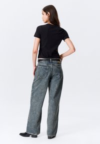 Μαύρο κοντό t-shirt συνδυασμένο με φαρδιά ξεβαμμένα μπλε τζιν, με υφή και κλασικό σχεδιασμό με πέντε τσέπες. Ορατά μαύρα μποτάκια αστραγάλου.
