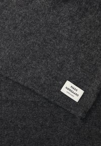 Grijze wollen sjaal met een zachte textuur. Heeft een wit label met "MADS NØRGAARD COPENHAGEN" in zwart gedrukt. Rechteckige vorm.