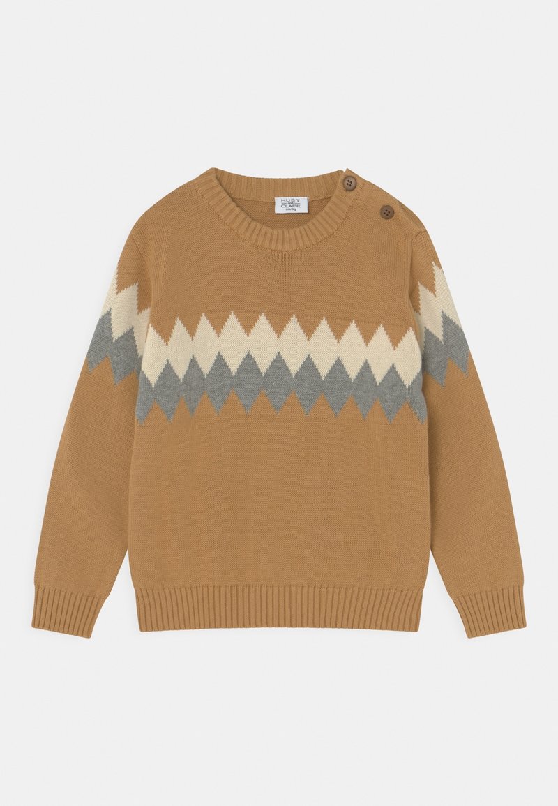 Pull en tricot marron clair avec un motif en zigzag blanc et gris sur la poitrine et les manches, comprenant deux boutons sur l'épaule gauche.
