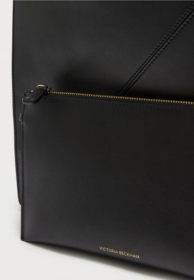 Poche d'un sac en cuir noir avec fermeture éclair dorée et petit logo Victoria Beckham embossé près du bord inférieur.