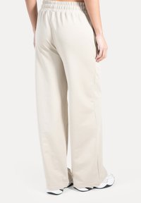 Beige bukser med vide ben, elastisk talje og blødt, let stof. Glat tekstur, indsnævrede ben og synlige sidelommer.