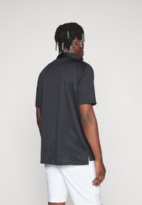 Svart kortermet poloshirt med krage, glatt tekstur, sidesplitt og avslappet passform, stylet med hvite shorts.