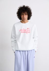 Sweatshirt branco com estampa gráfica rosa que diz "nike International Sportswear". Combinado com calças soltas em lavanda. Tecido suave, decote redondo.
