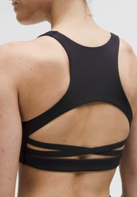 Kvinna som bär en svart sportbehå med racerback-design och korsade band på den nedre delen av ryggen, sedd bakifrån.